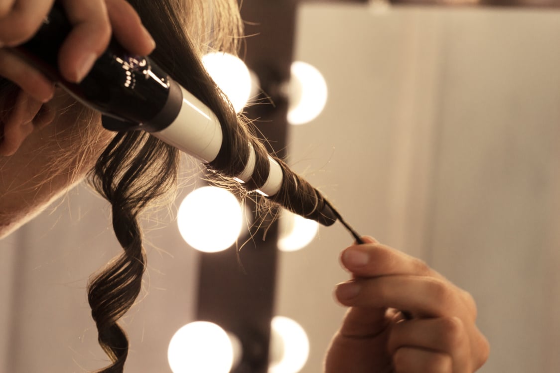 Hairstylist curling hair client in hairdressing salon